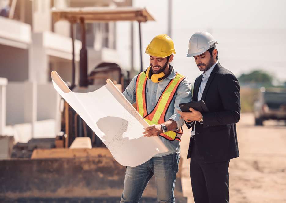Construction workers with blueprints at building site
